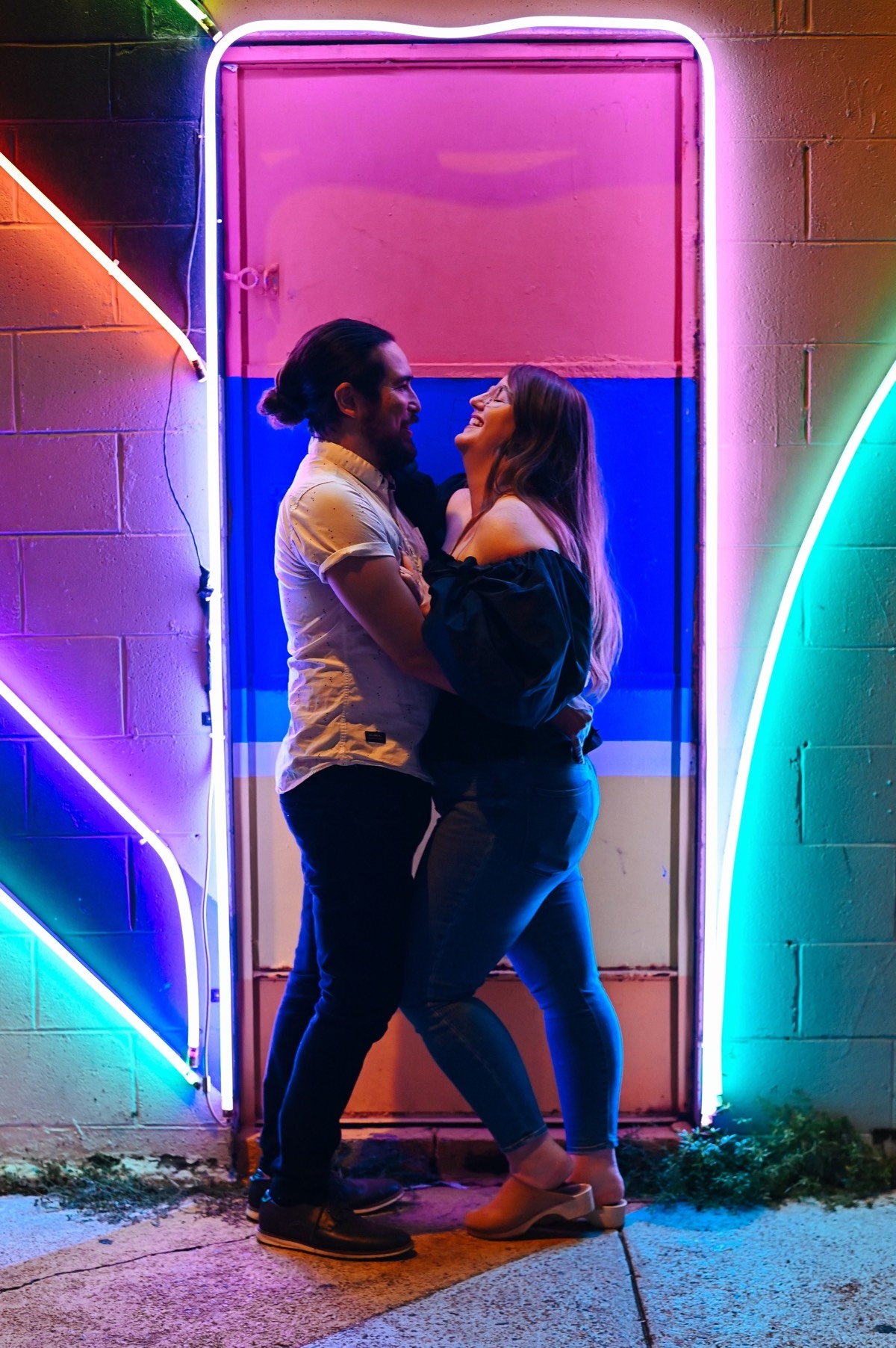 Nick and Colleen embracing and looking at each other happily in front of a neon art installation